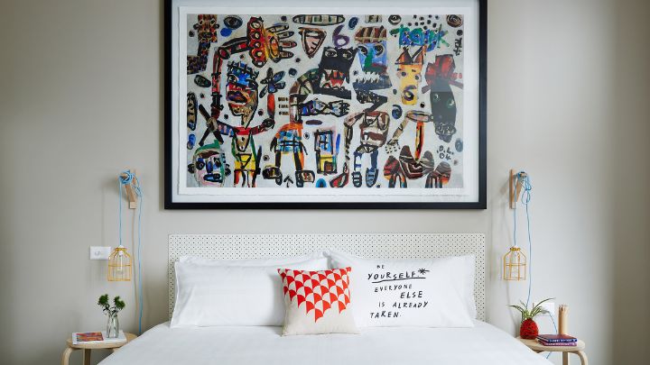 A king size bed with an orange blanket and a large abstract painting on the wall